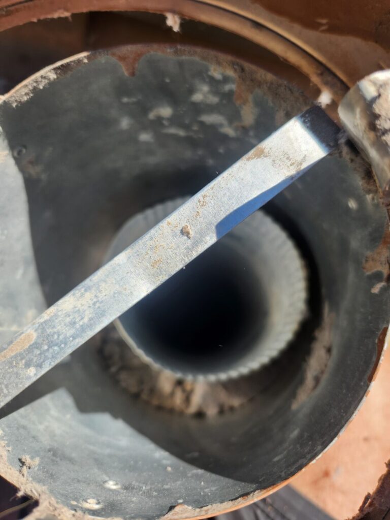 Dryer roof vent opening after lint removal, with a metal support bar across the opening.